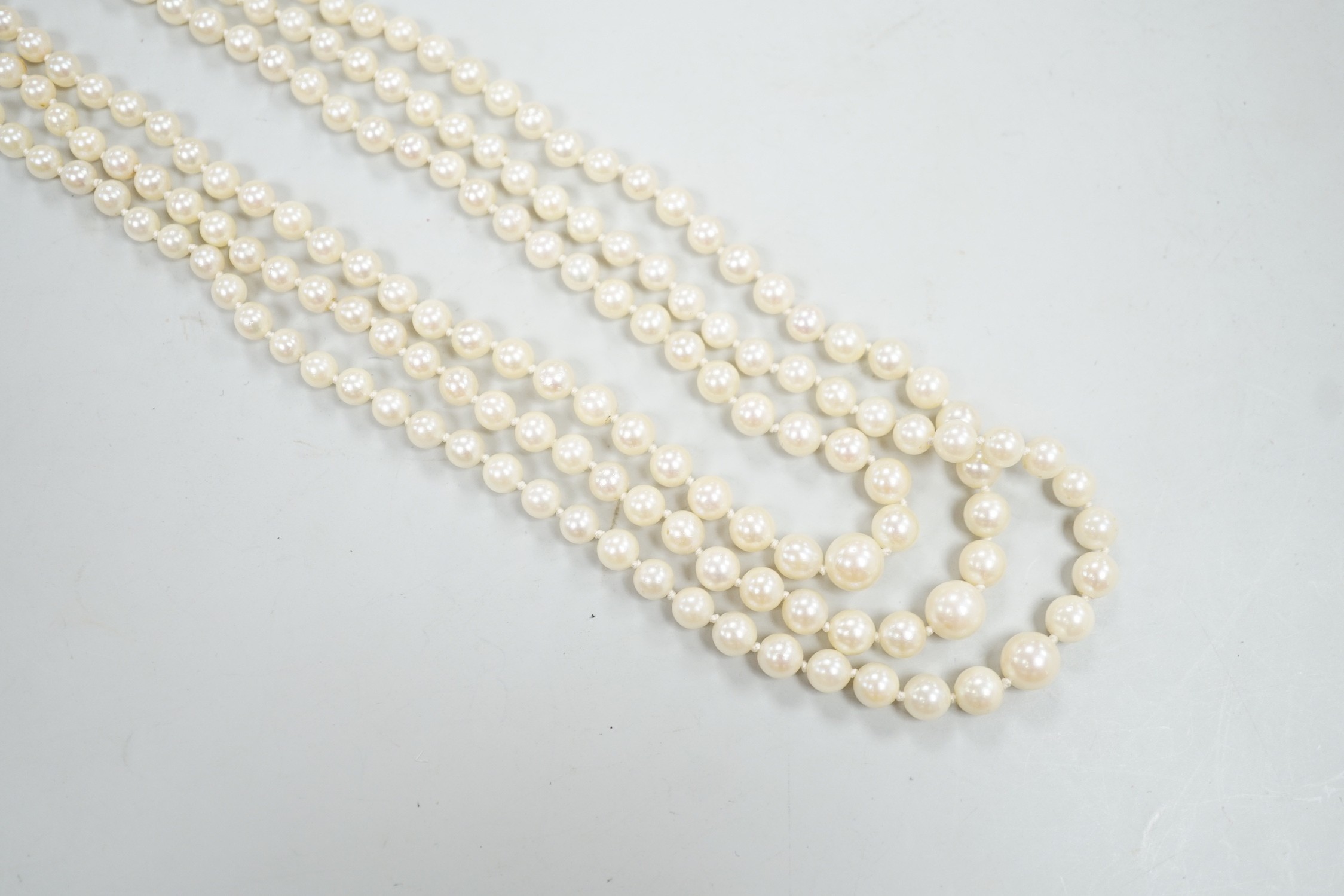 A 1960's triple strand graduated cultured pearl necklace, with 9ct white gold, ruby and diamond chip cluster set clasp, 49cm.